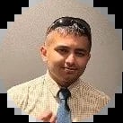 Professional headshot of a man wearing a beige blazer and blue tie against a neutral background