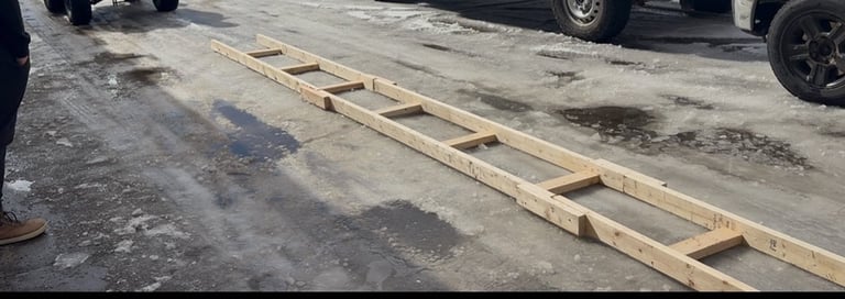 Wooden ladder or beam lying on a wet asphalt surface with parked vehicles in the background