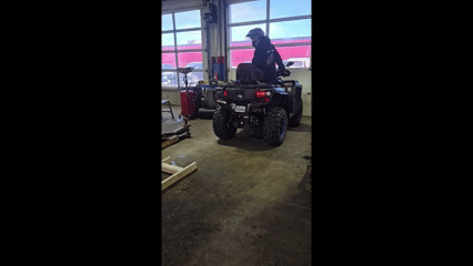 Person riding a red and black ATV indoors in a warehouse or showroom with large windows